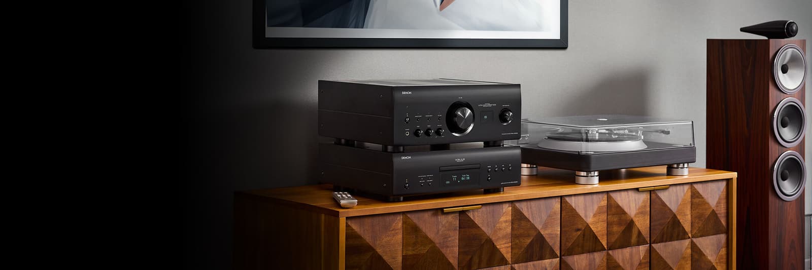 Stacked black Denon components beside a turntable and floor-standing speakers on a wooden cabinet.
