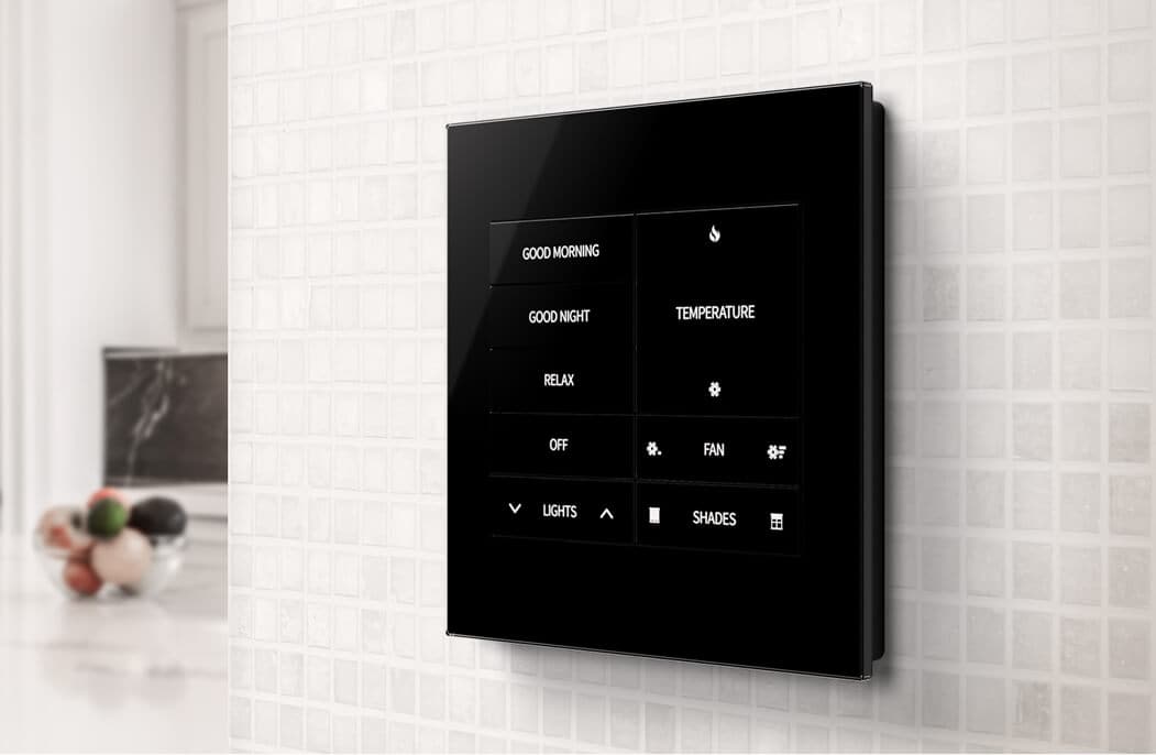 Black glass Crestron Horizon keypad on a mosaic-tiled wall in a bright kitchen, with lighting, climate and shade buttons.
