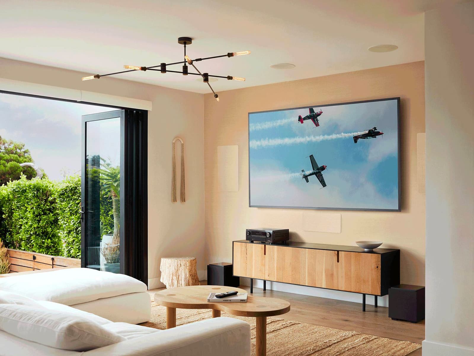 Denon AVR-X3800H on an oak sideboard in a bright open-plan living room with in-ceiling speakers and folding glass doors.