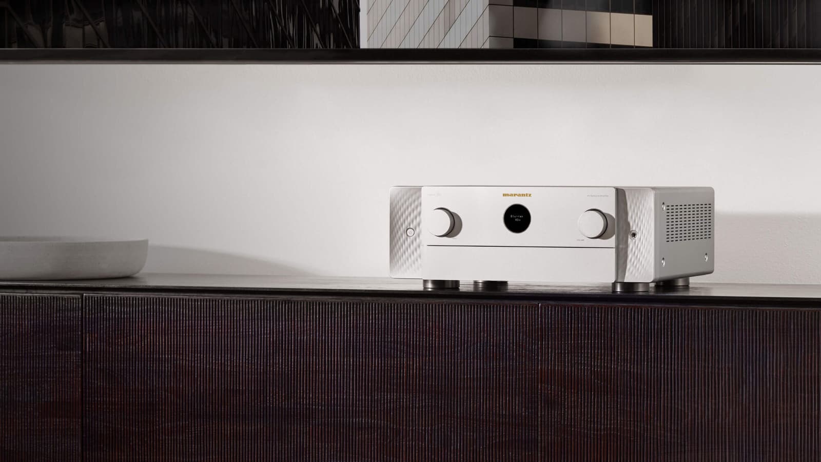 Marantz AV receiver in Silver-Gold on a dark ribbed-timber credenza in a minimal interior.